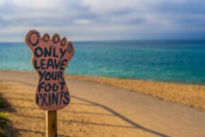 A wooden sign in the shape of a foot sits on the beach and represents the role of tourism consultants by stating, "only leave your footprints."