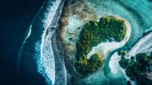 small, remote island with lush vegetation and white foam waves crashing on all sides