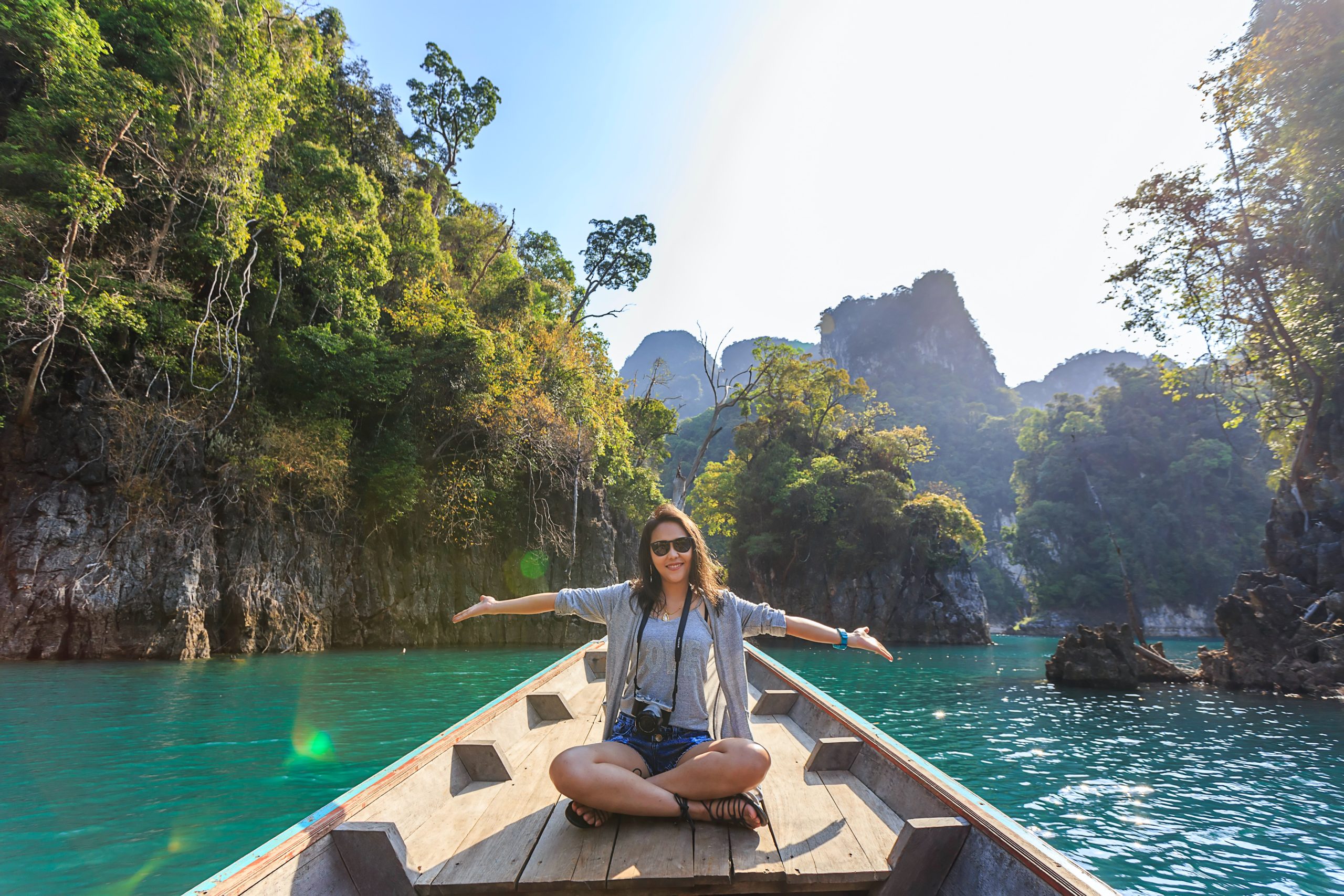Tourist in sunglasses sits on a boat in Thailand surrounded by trees and nature